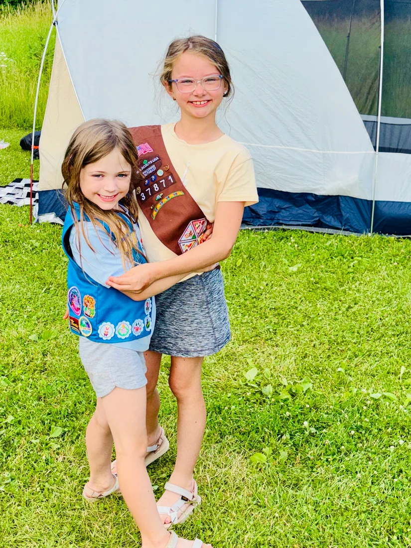 Addie and Ellie hugging beside a camping tent
